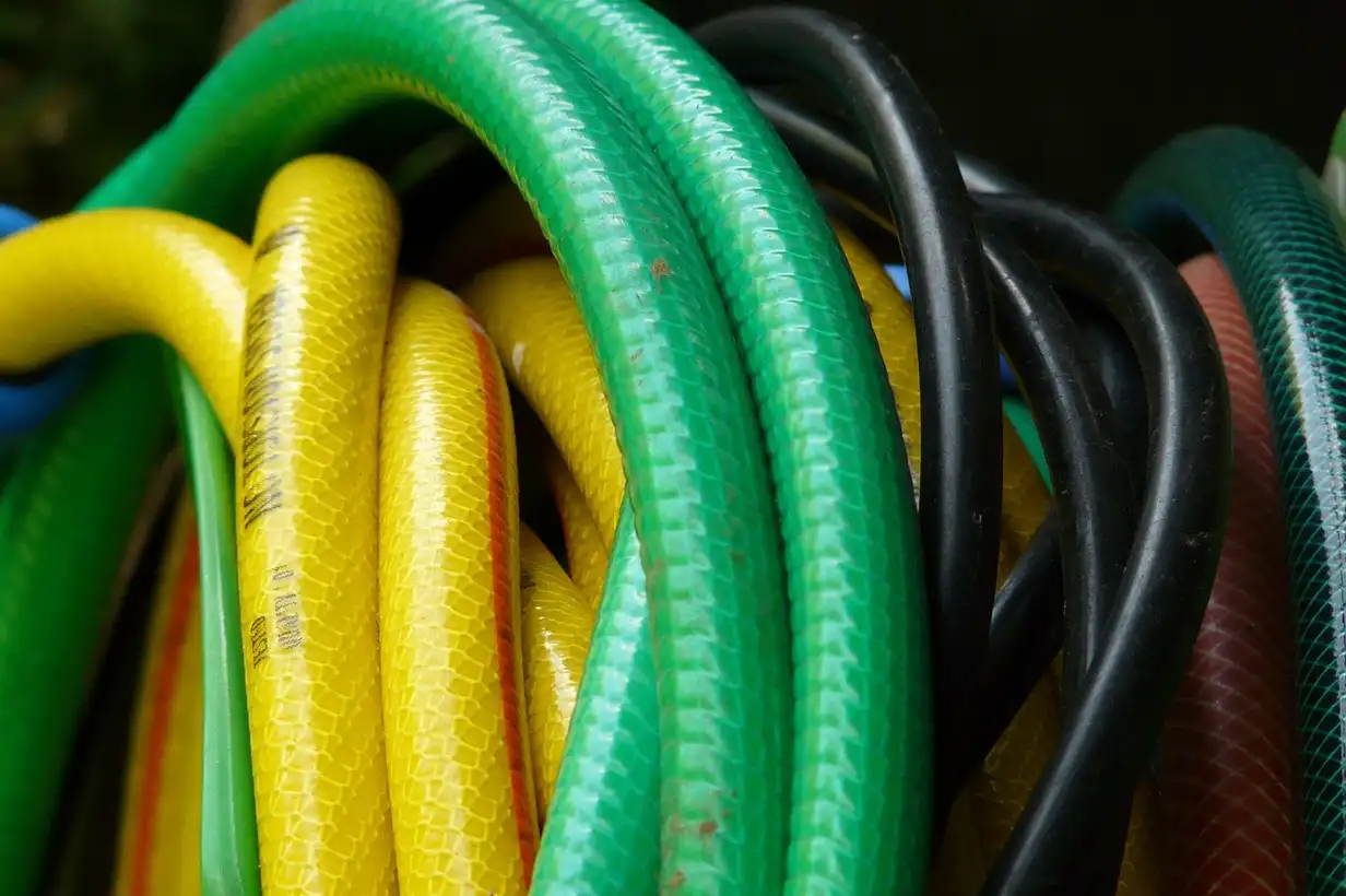 Tuyau d’arrosage déroulé sur une pelouse, raccordé à un robinet de jardin, prêt à arroser les massifs et le potager