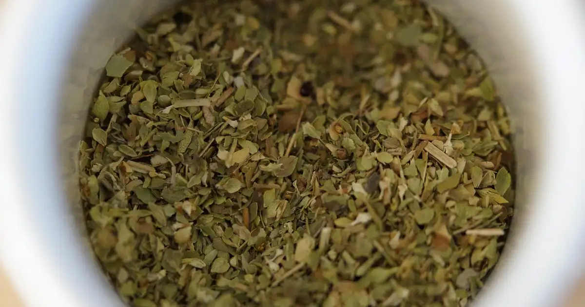 Feuilles sèches d'origan dans un bol en bois à côté de branches fraîches, prêtes pour des recettes en cuisine